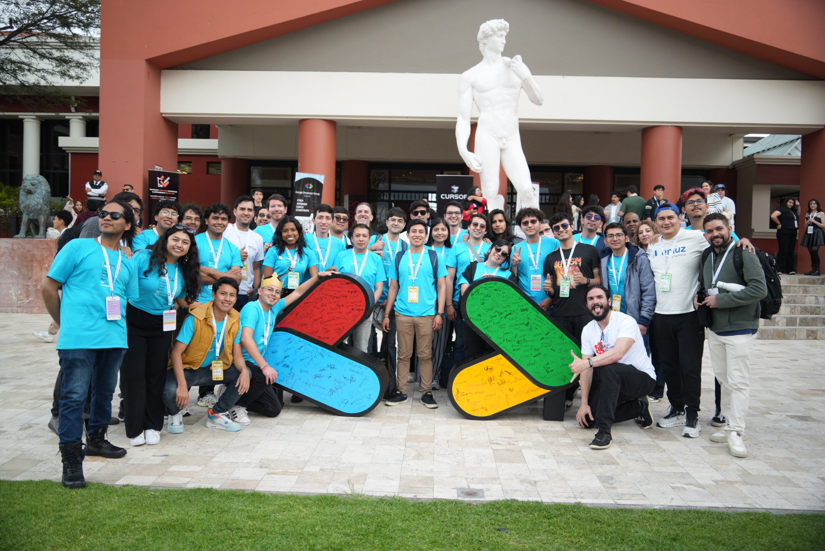 Comunidad de DevFest Quito posando con props del logo de GDG frente al campus USFQ